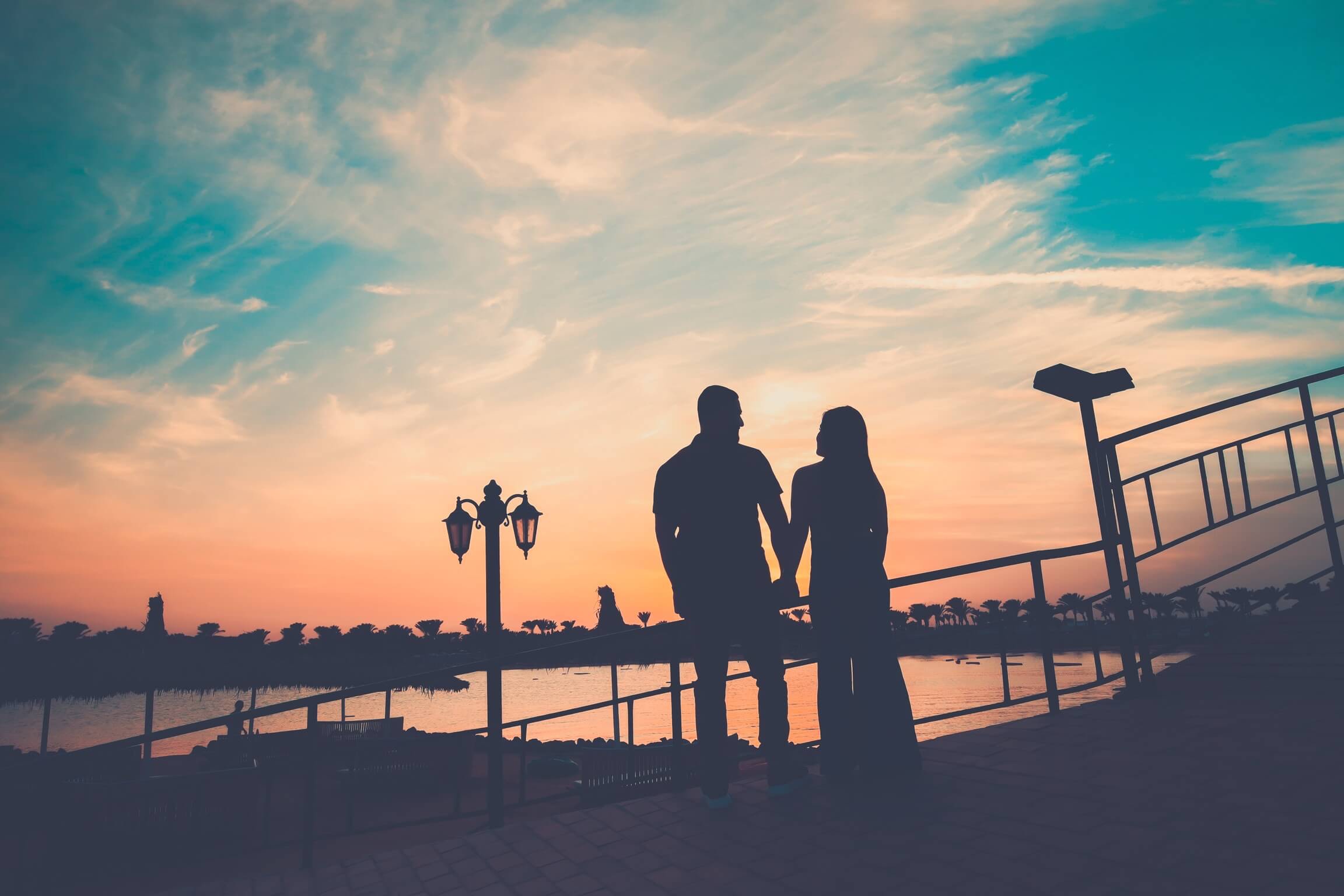 Sunset Reflections: A Couple's Embrace - Couple sitting close together in silhouette.