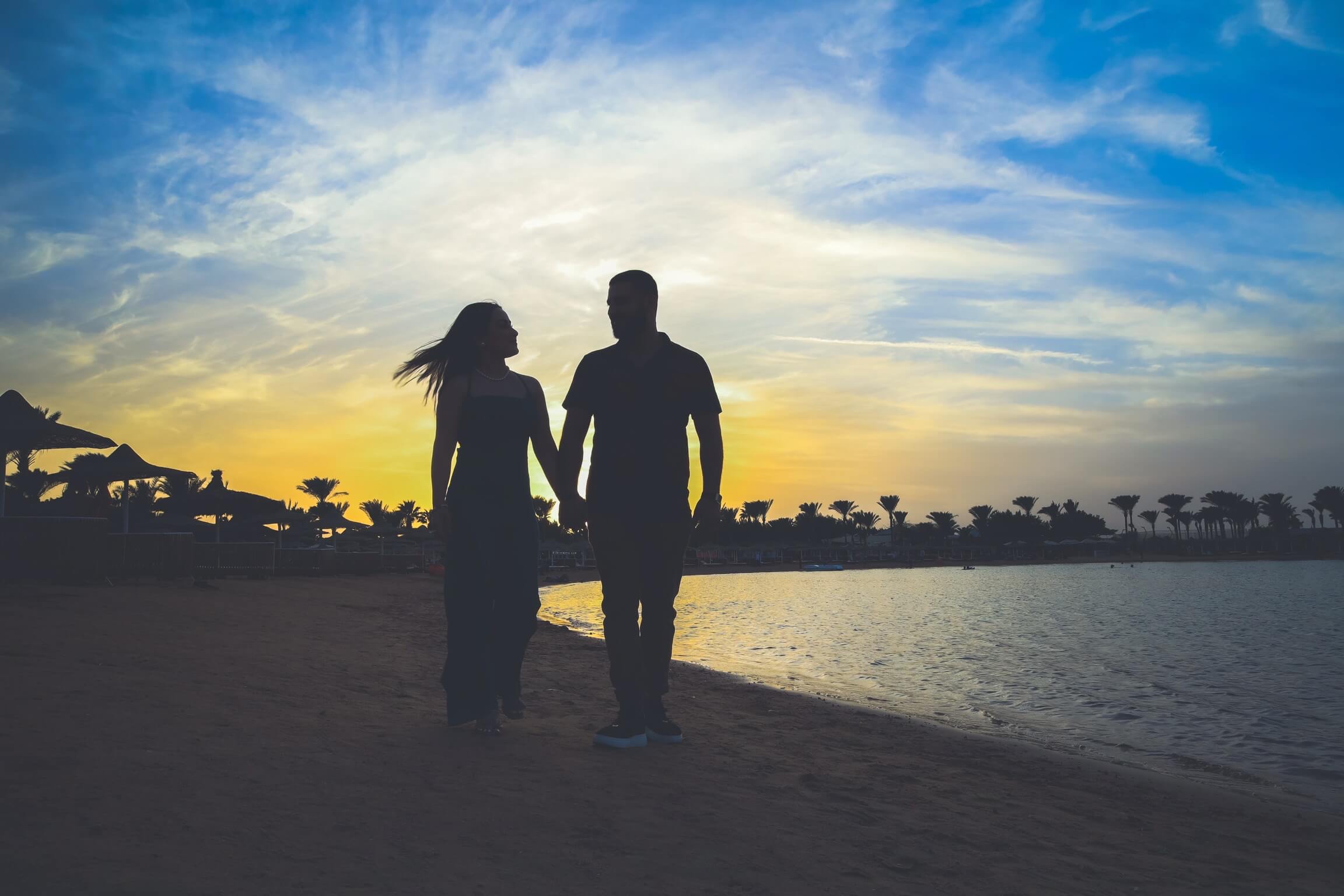 A Sunset Stroll for Two - Couple walking hand-in-hand along the coastline.