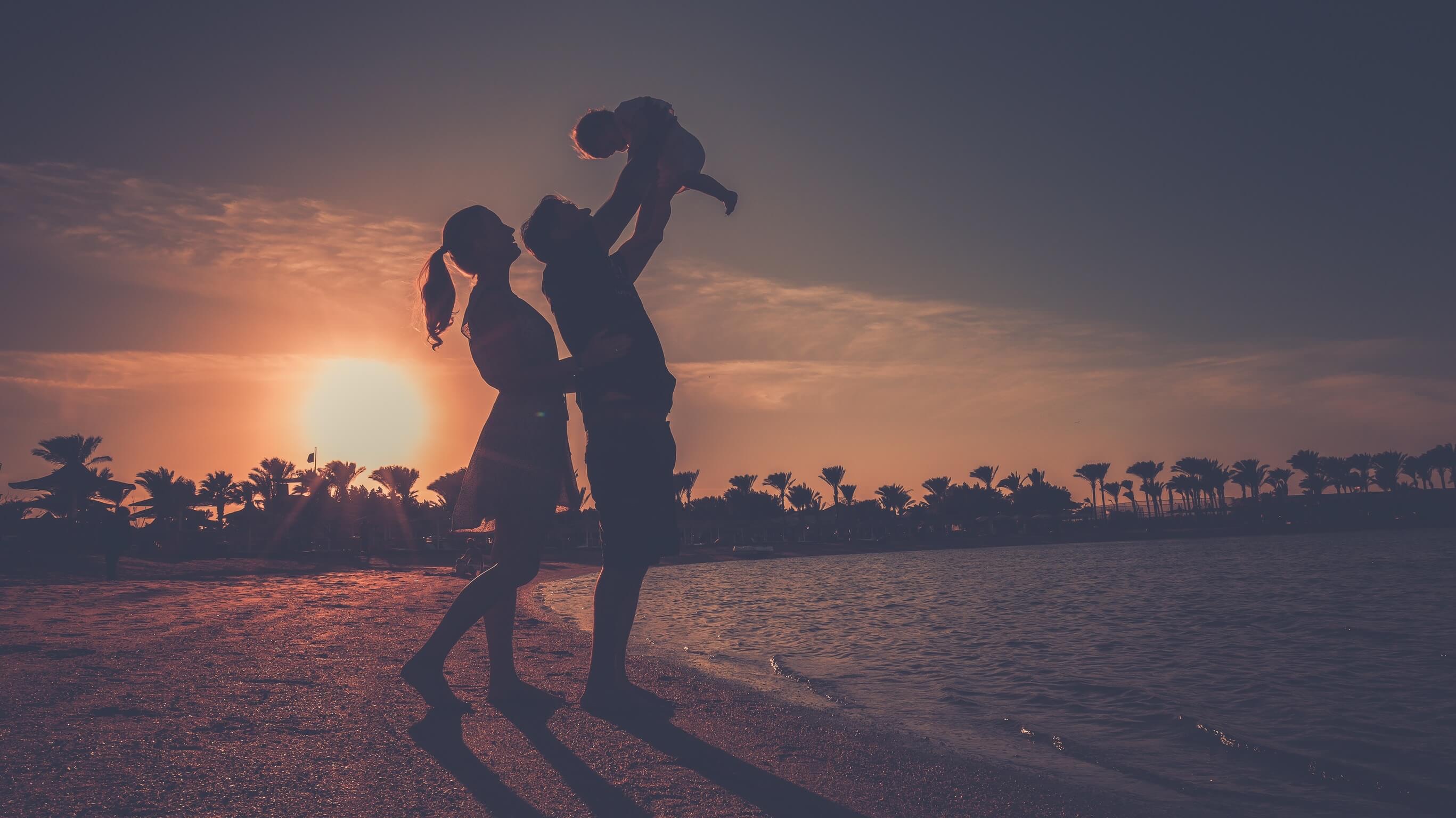 Silhouette of parents joyfully lifting their child at the beach during sunset, photographed by Kareem Ahmed at Desert Rose Resort.