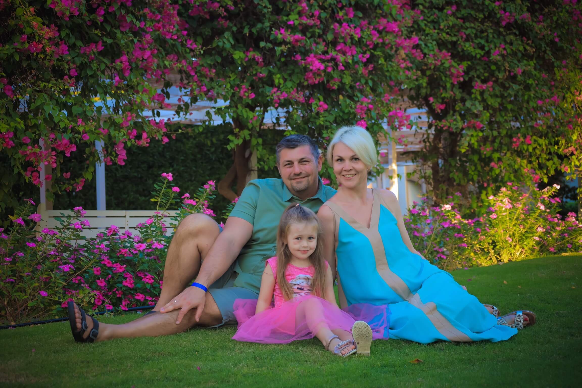 A happy family—father, mother, and young daughter—posing together and smiling in a beautiful garden full of colorful flowers in Hurghada, Egypt.